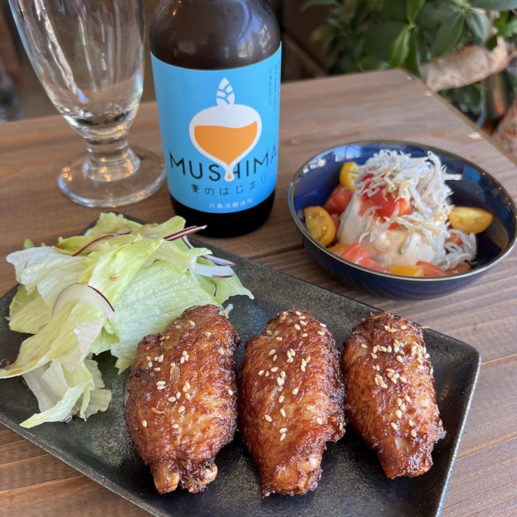 地ビールのボトルとトマトの小皿料理や手羽元を使った料理などのおつまみ