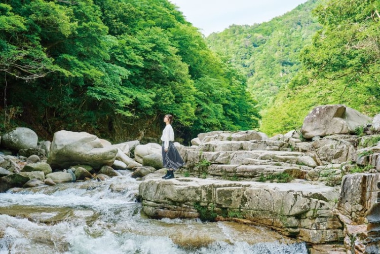 森を背景に川沿いに立つ女性