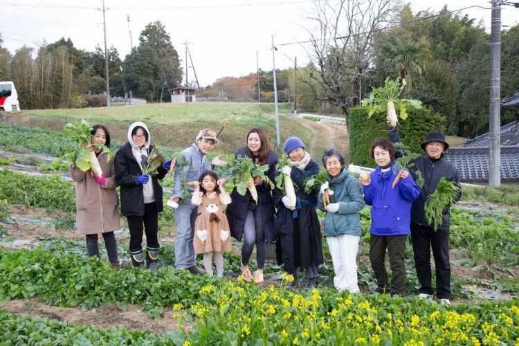 大根などのつくった野菜を手に持ってる大人や子ども