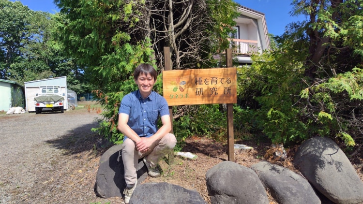 研究所の看板の前に座る日向優さん