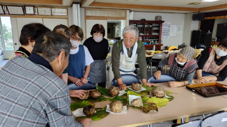 こんにゃくイモが並んだテーブルを囲む人達