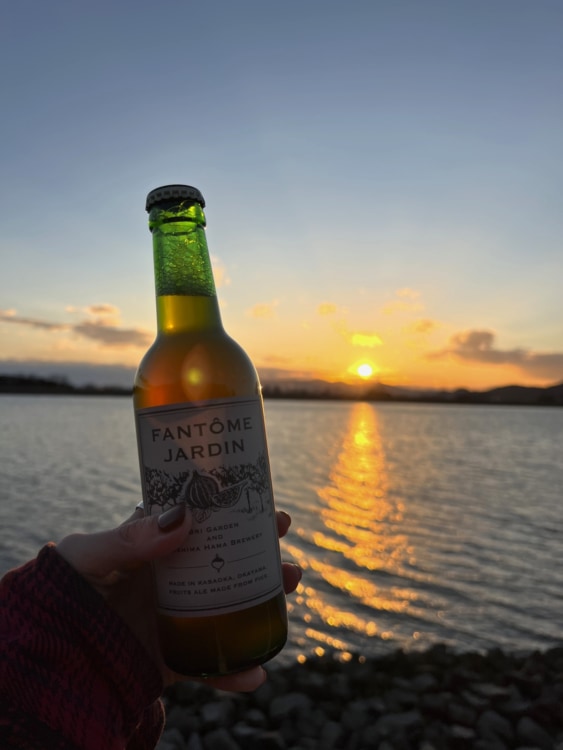 海にのびる夕日と並ぶようにビールを手に持ってる