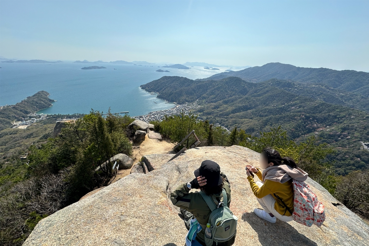 山頂に座る人が瀬戸内海の絶景を眺めている