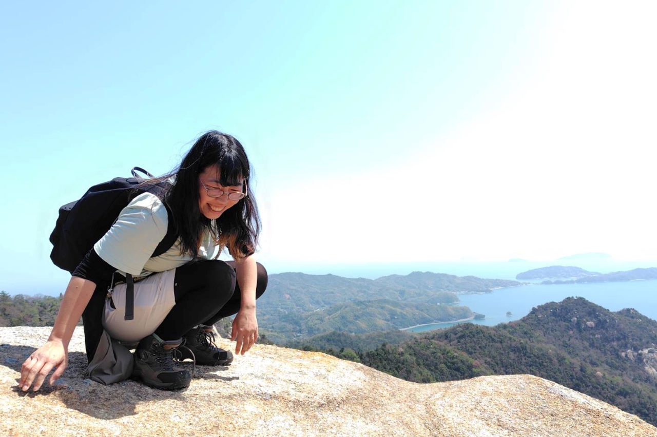 海が見渡せる山の岩の上で女性がしゃがんでいる